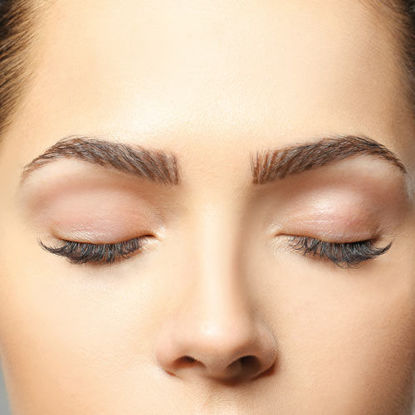 Nahaufnahme eines weiblichen Gesichts mit geschlossenen Augen, perfekt gestylten Augenbrauen und dezentem Make-up, Fokus auf der Augenpartie.